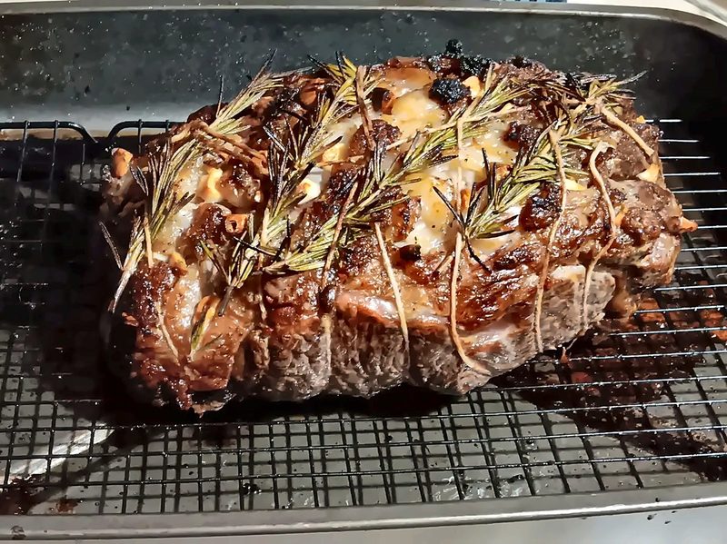 A tied beef roast crusted with rosemary sprigs and garlic, resting on a rack